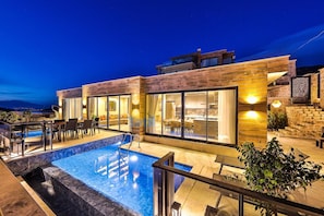 Een modern huis met een zwembad, buitenmeubels en grote ramen.