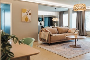 A modern living room with a sofa, a dining table, and a kitchen in the background.