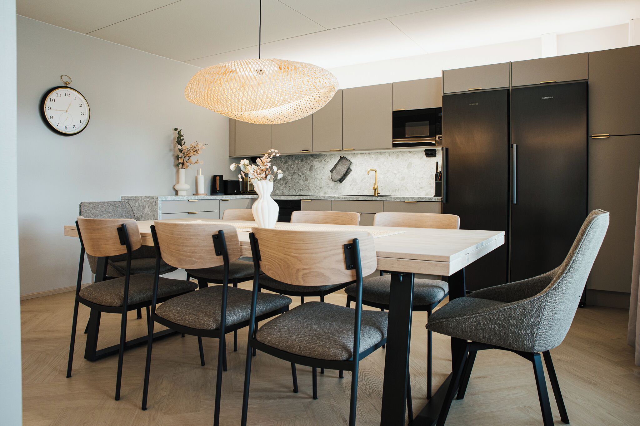 Una cocina moderna con comedor, que incluye una mesa redonda, seis sillas, un refrigerador negro y una lámpara colgante.