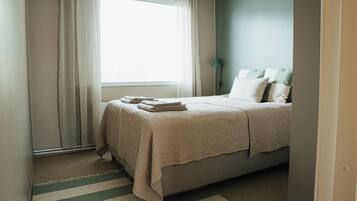 A bedroom with a bed, a window with curtains, a bedside lamp, and a striped rug.