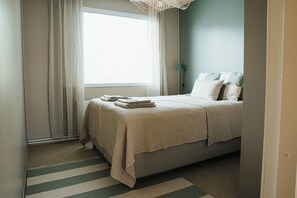 A bedroom with a bed, a window with curtains, a bedside lamp, and a striped rug.