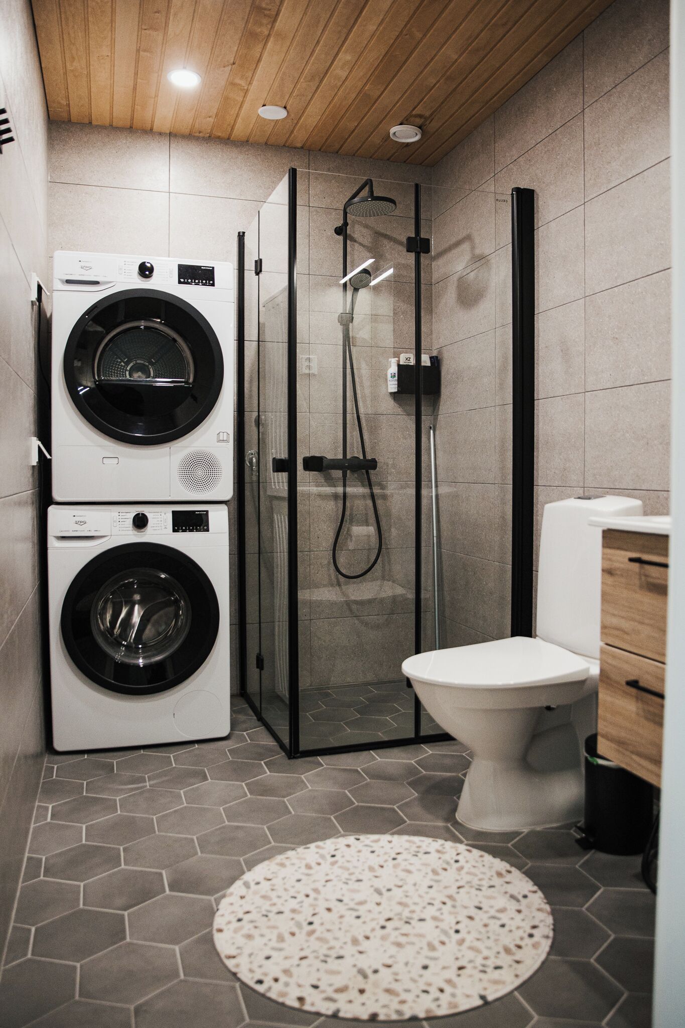 A compact bathroom with a washing machine, a glass-enclosed shower, and a toilet.
