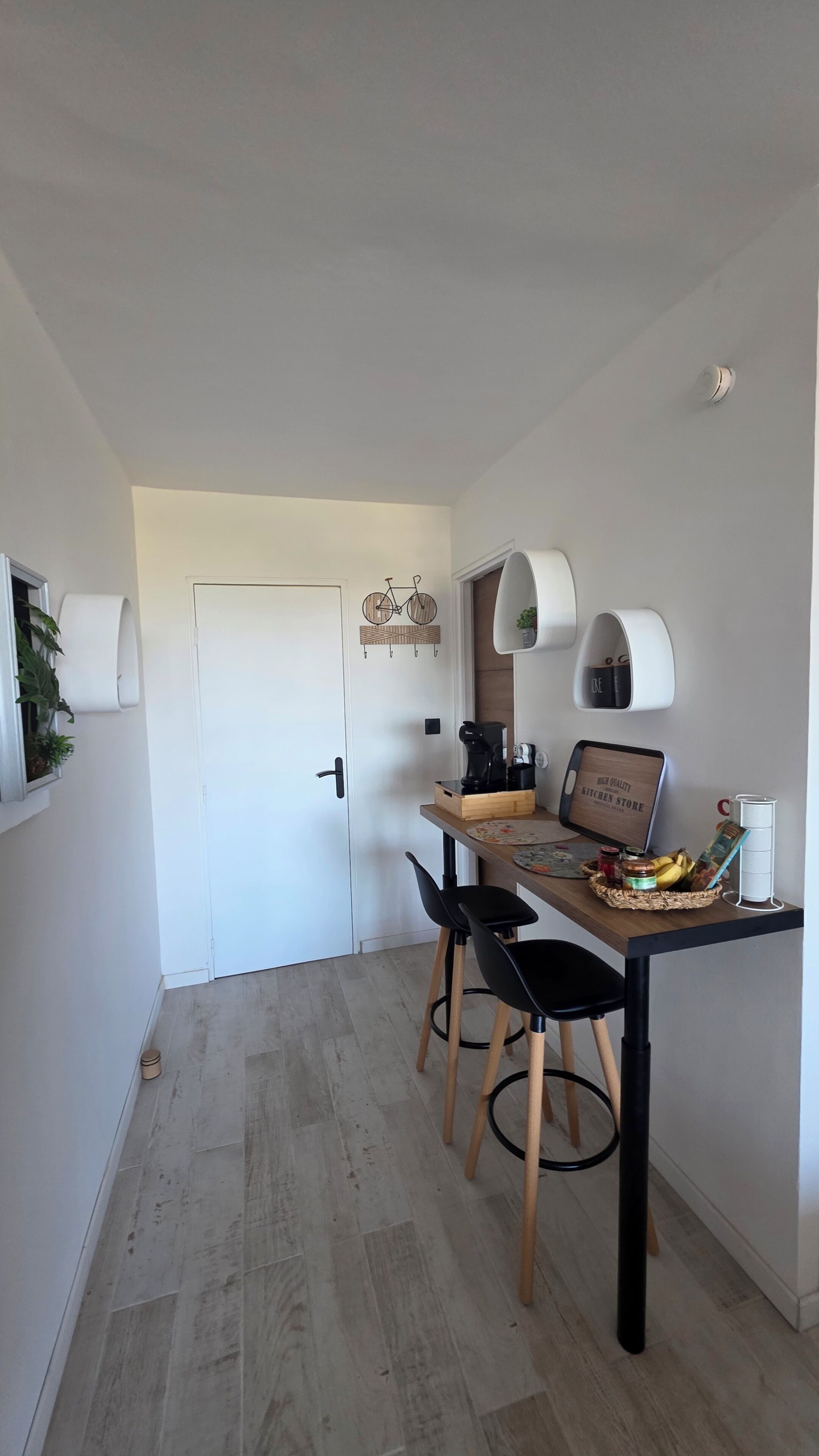Une cuisine moderne avec une table en bois, des chaises noires et une machine à café.