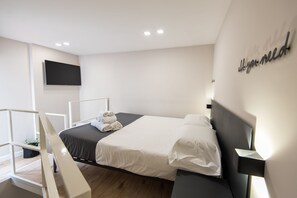 Ein modernes Hotelzimmer mit einem Bett, einem flachbildfernseher an der Wand und einem Nachttisch mit Lampe.