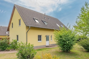 A two-story house with a sloped roof, multiple windows, and a door. - Modern vacation home in Korswandt with a garden, fireplace, and a view of the lake nearby (Korswandt)