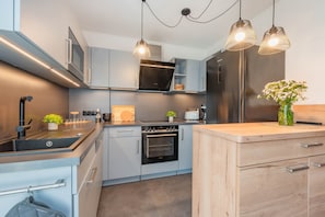 Een moderne keuken met roestvrijstalen apparatuur, een houten aanrecht en hangende lampen.