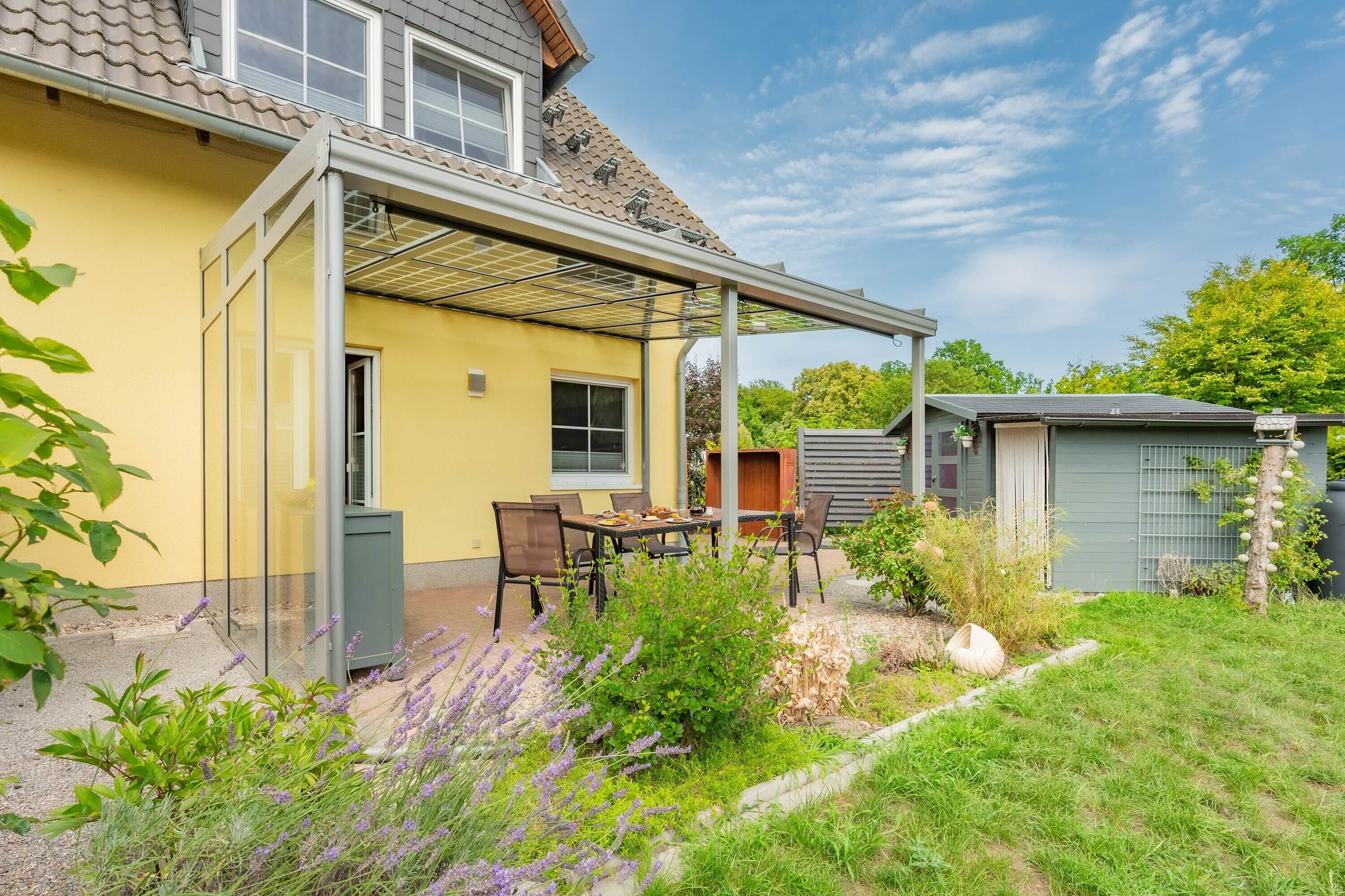 A yellow house with a covered patio, a small shed, and a garden with lavender.