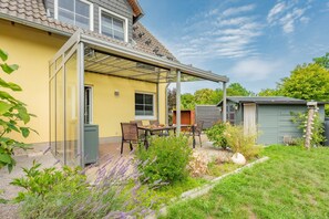 Een geel huis met een overdekte patio, een kleine schuur en een tuin met lavendel.