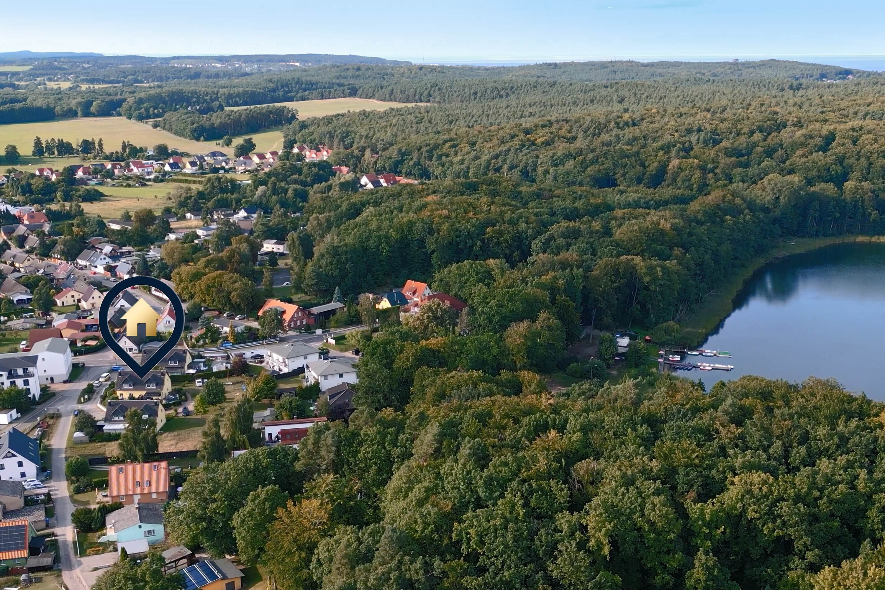 An aerial view of a residential area with houses, a lake, and a forested hill.