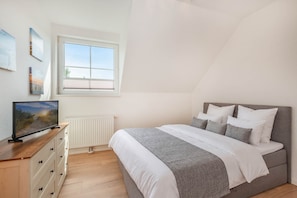 Een slaapkamer met een bed, een dressoir, een raam en kunstwerken aan de muur.
