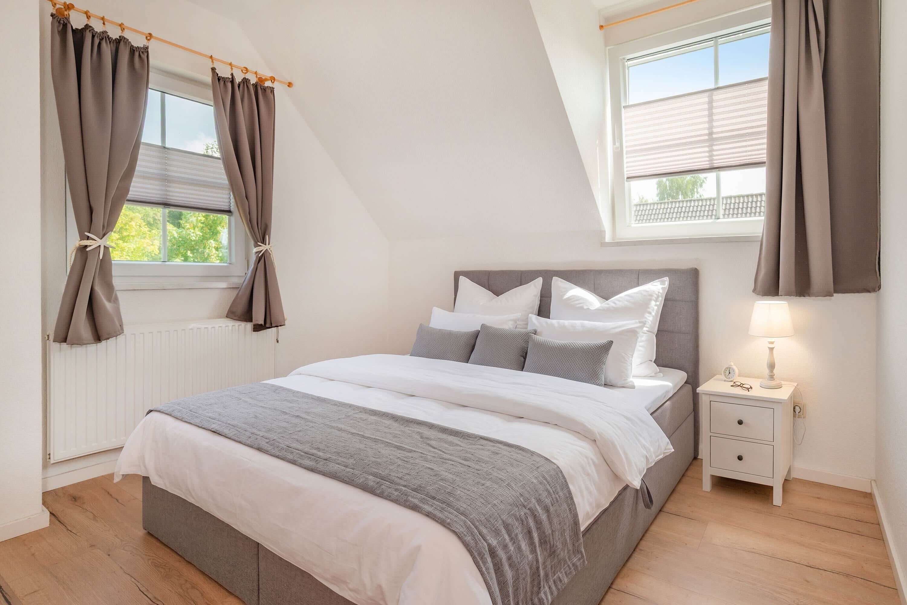 Un dormitorio con cama, mesita de noche, lámpara y cortinas.