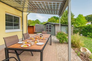 Un espace extérieur aménagé pour prendre les repas, avec une table dressée pour le petit-déjeuner, entourée de chaises, et une terrasse couverte.