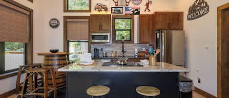 A modern kitchen with a central island, bar stools, wooden cabinets, and various kitchen appliances.