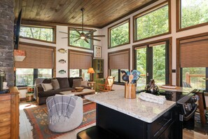 A spacious living area with a large window, a ceiling fan, and a kitchen with a stove. - Gorgeous new 1 bedroom with king bed, outdoor firepit, hot tub, lots of light! (Sevierville)