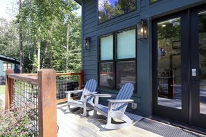 A wooden deck with two Adirondack chairs and a metal railing. - Gorgeous new 1 bedroom with king bed, outdoor firepit, hot tub, lots of light! (Sevierville)