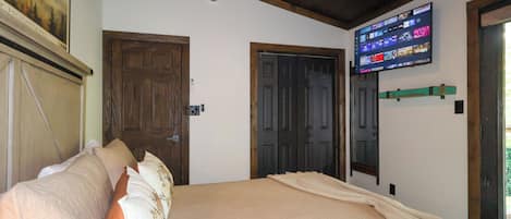 A bedroom with a bed, two doors, a mounted TV, and a painting on the wall.