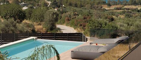 A rooftop pool with a clear view of the sea and a hilly landscape in the background.
