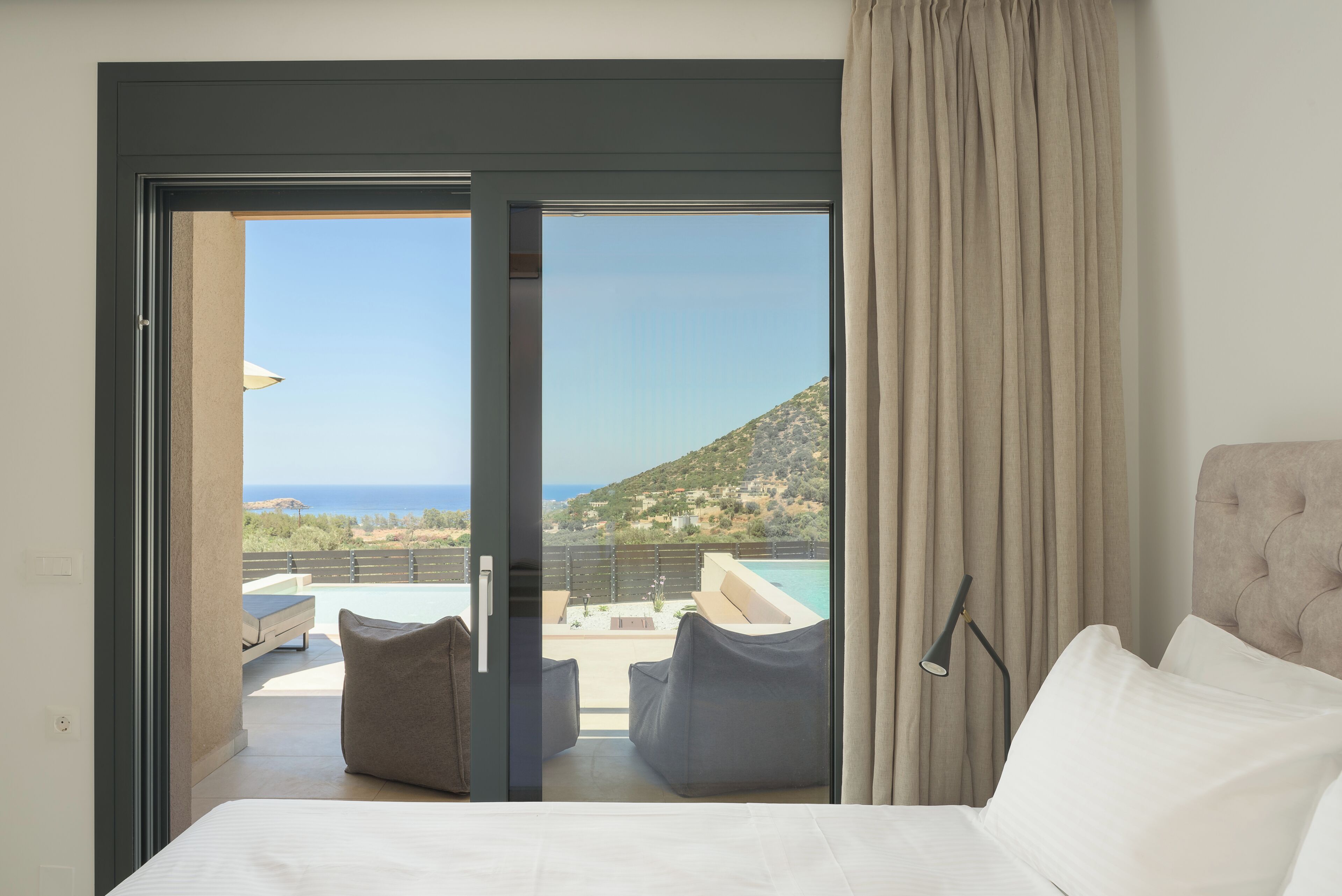 A hotel room with a bed, a view of a pool and hillside, and a sliding glass door.