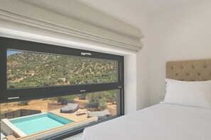 Ein Schlafzimmer mit großem Fenster, Bett und Blick auf Pool und Landschaft.