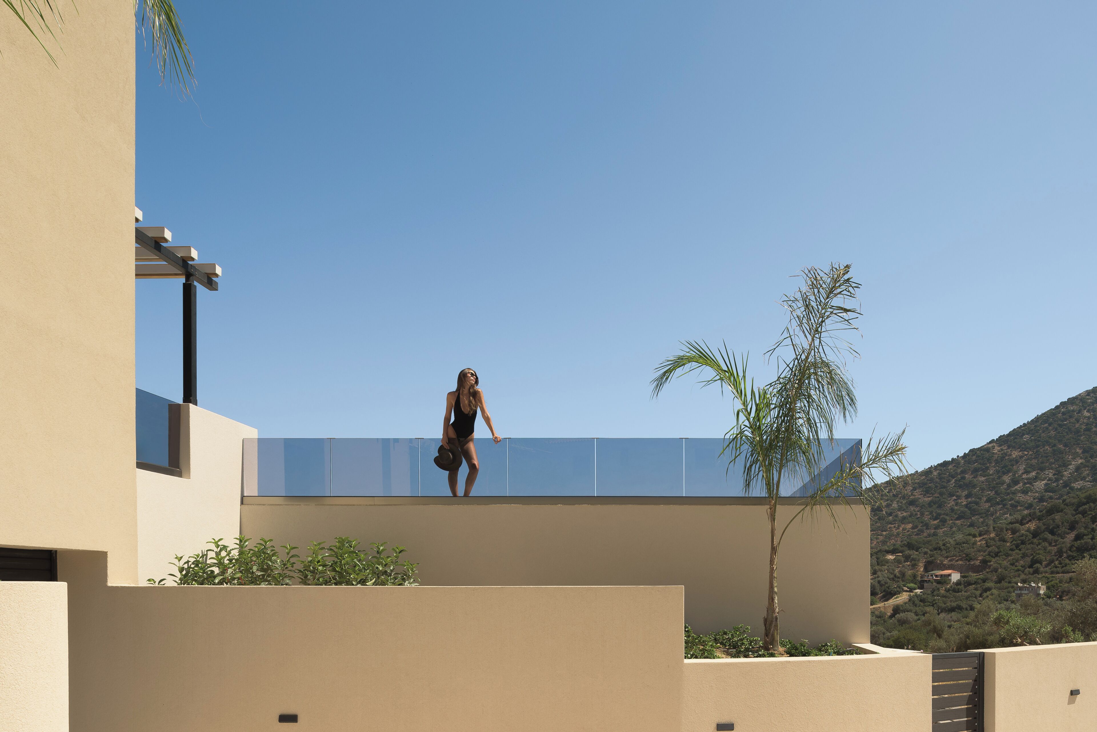 A modern building with a flat roof, a balcony, and a view of a hilly landscape.