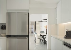 Eine moderne Küche mit einem eingebauten Edelstahlkühlschrank, weißen Schränken und einem Essbereich mit einem weißen Tisch und Stühlen.
