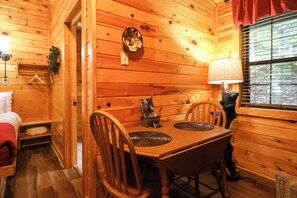 A wooden interior with a dining table, chairs, a lamp, and a bear statue. - Studio cabin- Firepit, hot tub, near the river, hiking trails, horseshoes! (Sevierville)