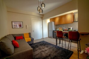 A modern living room with a grey sofa, red and yellow cushions, a black rug, and a dining area with two red chairs. - 4.97 Super Host`s New Boutique & Prime Location (Limassol)