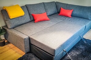 Ein graues Sofa mit roten und gelben Kissen, eine schwarze Stehlampe und ein Blumentopf.