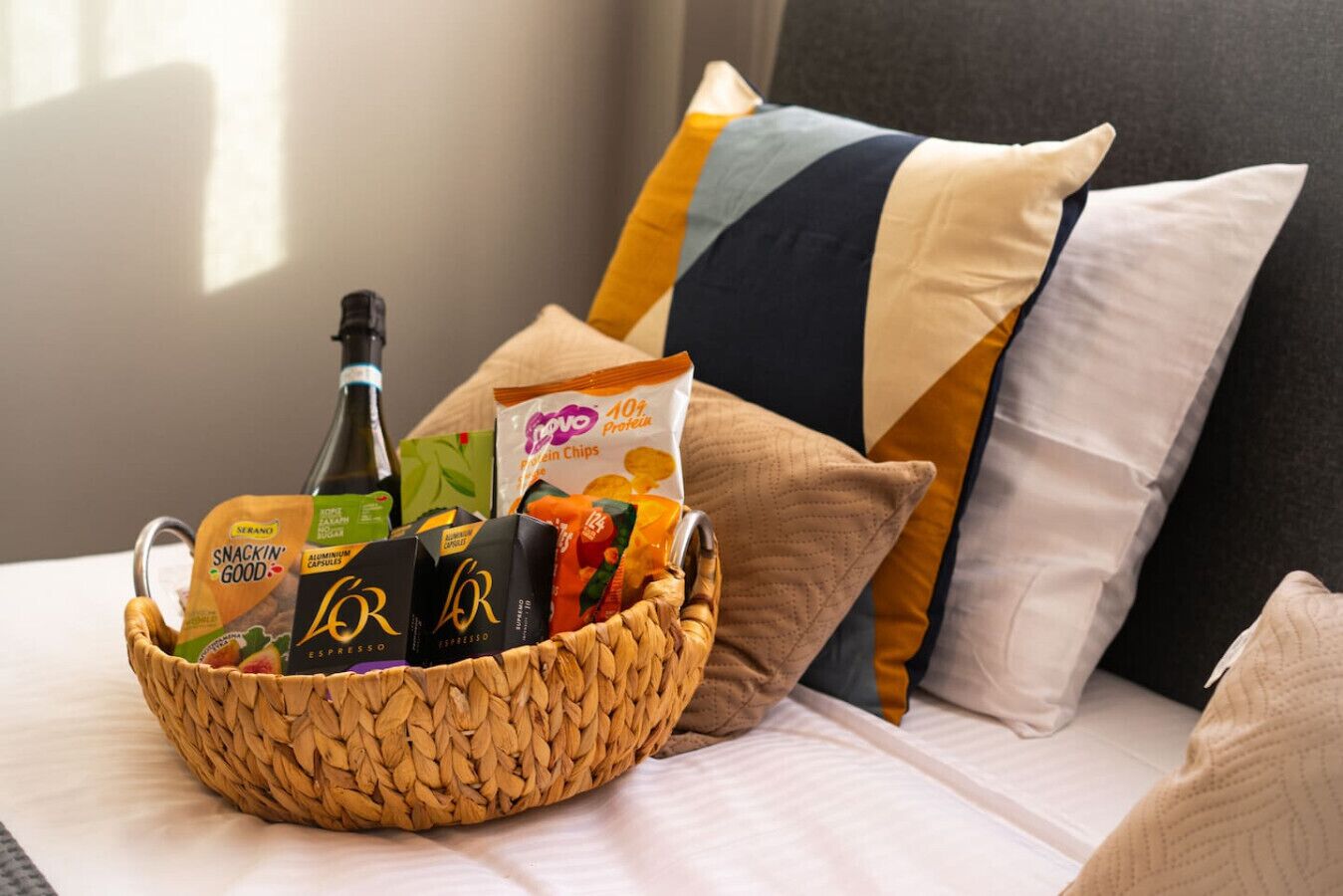 Un panier rempli d’en-cas et de boissons, posé sur un lit avec des oreillers.