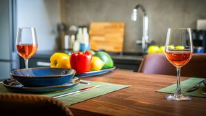 Una mesa de comedor con dos copas de vino, un cuenco de fruta y una tabla de cortar de madera en una cocina moderna.