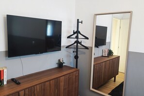 Ein Zimmer mit einem Wandfernseher, einem Holzschrank, einem Spiegel und einem Kleiderhaken.