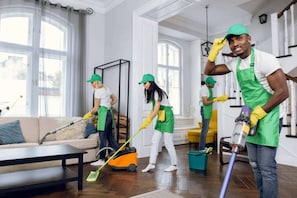 Eine Gruppe von Menschen räumt einen Raum mit einem Sofa, einem Couchtisch und einem Fenster mit Vorhängen auf.