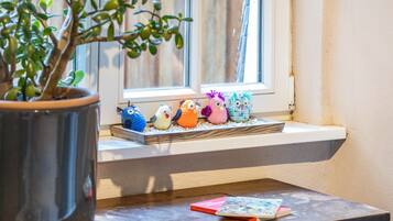 A window sill with a row of colorful knitted animals, a potted plant, and a small table with books.