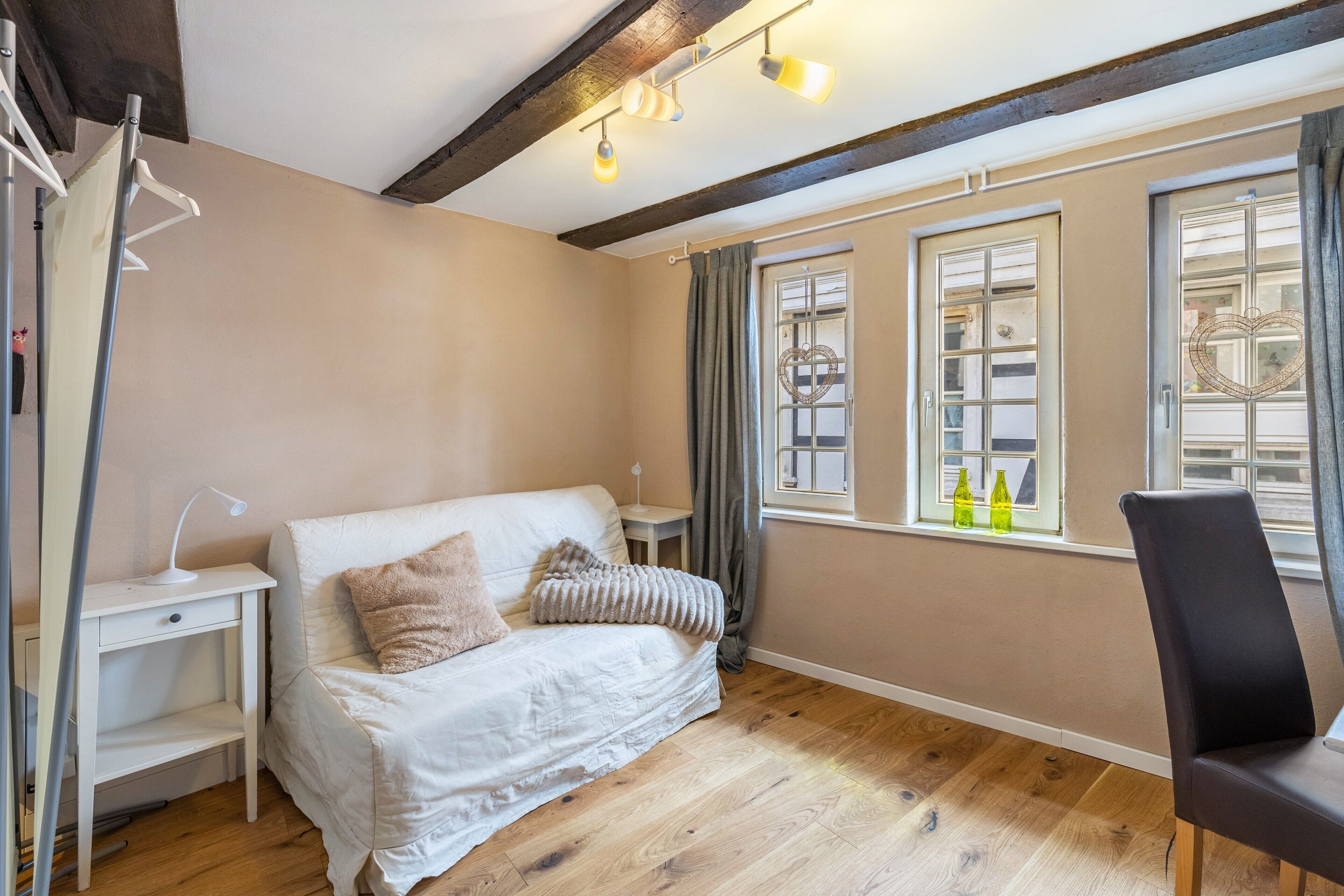 Ein Zimmer mit einem Bett, einem Sessel, einem Schreibtisch und einem fenster mit Vorhängen.