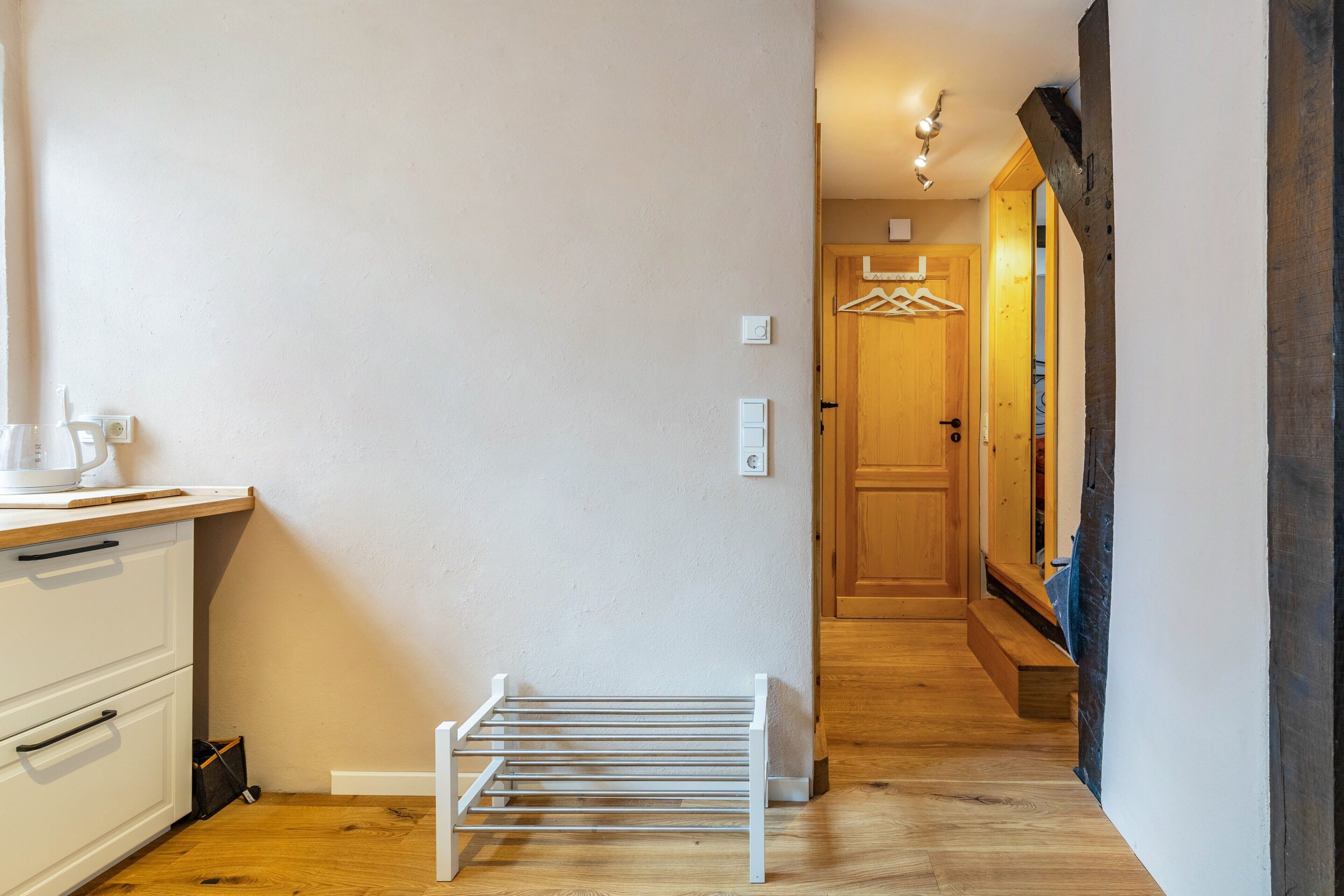 A narrow hallway with a white drying rack, a wooden door, and a light fixture.
