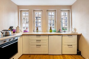 A kitchen with a stove, oven, and a dishwasher. There are three windows with curtains.