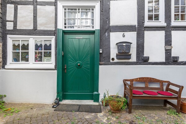 A green door with a window above it, a wooden bench with red cushions, and a potted plant on the ground.