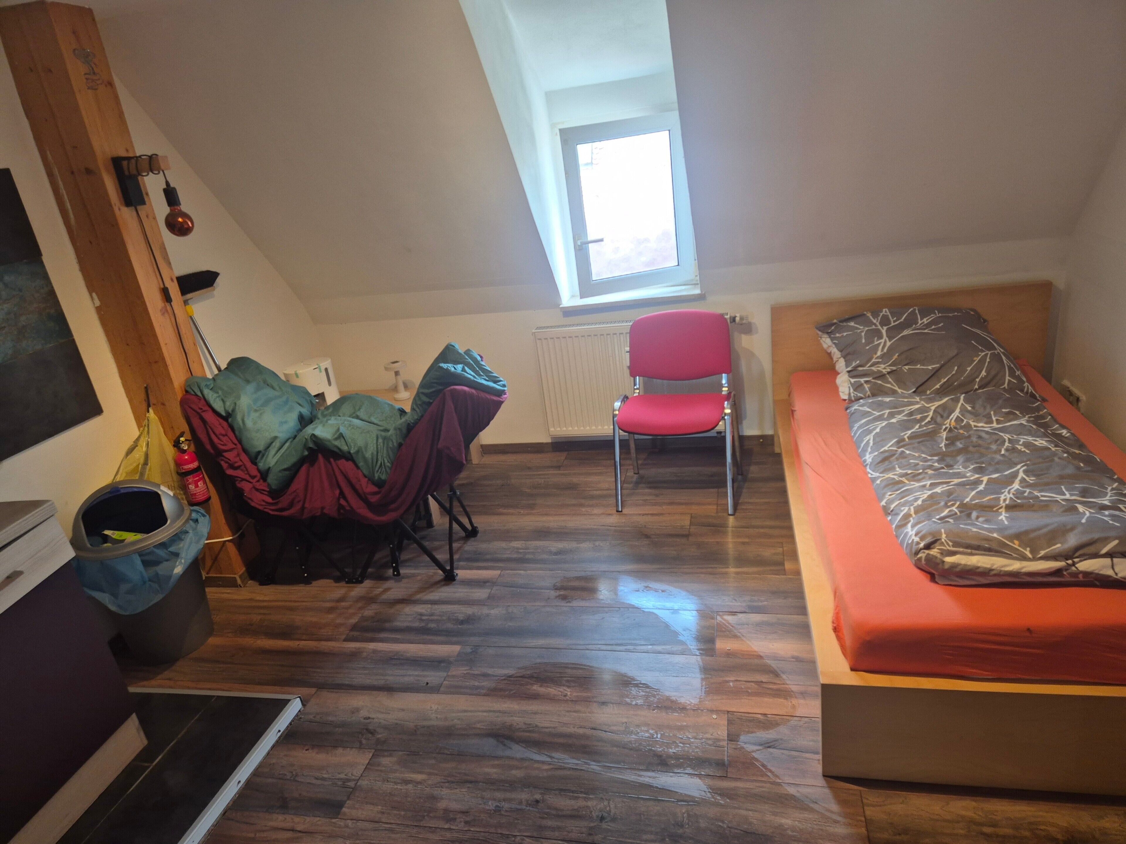 Une petite pièce, de taille modeste, comprenant un lit simple, une chaise, un radiateur et une fenêtre.