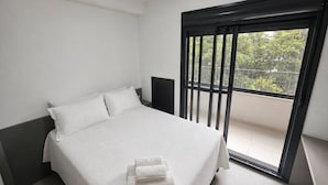 A bedroom with a bed, a nightstand, and a balcony with a view. - Studio Completo - Aclimação (São Paulo)