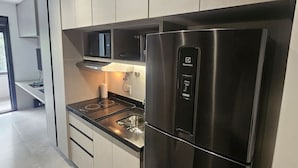 A modern kitchen with stainless steel appliances, including a refrigerator and microwave, and light-colored cabinetry. - Studio Completo - Aclimação (São Paulo)