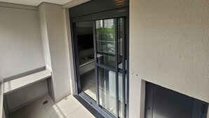 A balcony with a glass door leading to an outdoor area, a ceiling light, and a textured wall. - Studio Completo - Aclimação (São Paulo)