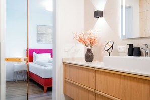 Een moderne hotelkamer met een bed, nachtkastje en een badkamer met spiegel, wastafel en toiletartikelen.