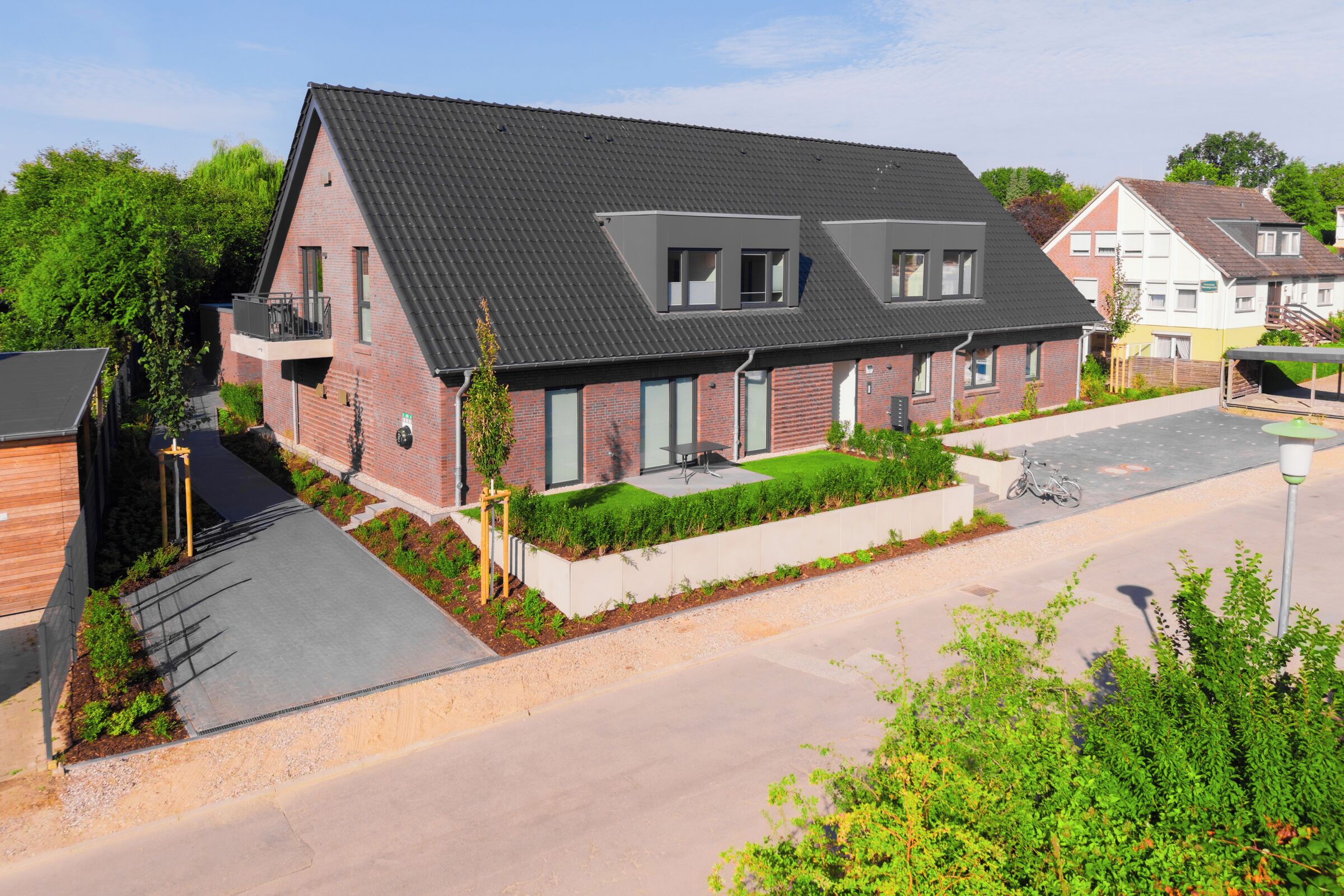 A two-story residential building with a sloped roof, a balcony, and a small garden area.