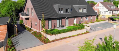 Un immeuble résidentiel de deux étages, doté d’un toit en pente, d’un balcon et d’un petit jardin.