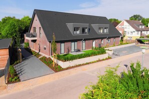 A two-story residential building with a sloped roof, a balcony, and a small garden area. - Wind Force 7 - Sea State. Sauna. Patio. Dog-Friendly (Grömitz)