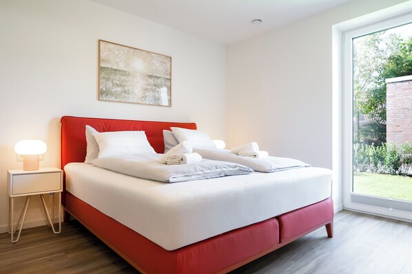 Un dormitorio moderno con cabecera roja, ropa de cama blanca y una lámpara de noche.