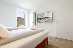 A bedroom with a bed, a door, and a wall-mounted TV displaying a beach scene.