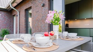 A dining table set with white tableware, a vase of flowers, and apples. - Wind Force 7 - Sea State. Sauna. Patio. Dog-Friendly (Grömitz)
