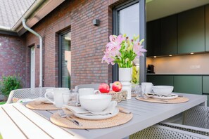 A dining table set with white tableware, a vase of flowers, and apples. - Wind Force 7 - Sea State. Sauna. Patio. Dog-Friendly (Grömitz)
