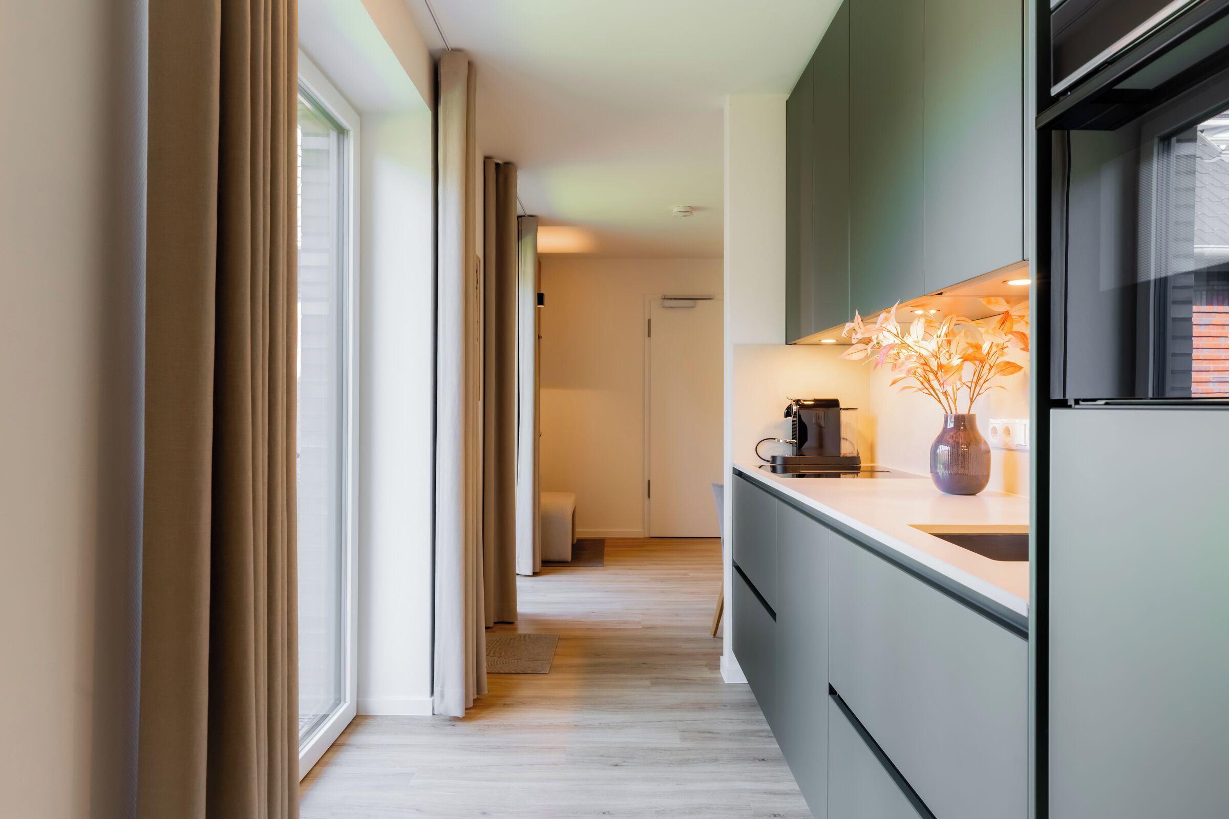 A modern kitchen with a built-in oven, a coffee machine, and a vase on the counter.